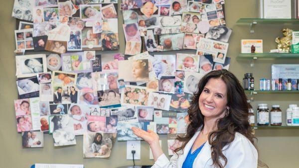 Denise, The Fertility Godmother, showing off her famous wall of babies she helped bring into the world.