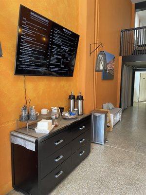 Digital menu above the coffee and utensil station.