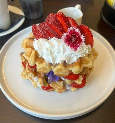 Freshly made waffle, juicy strawberries, whipped cream, and an edible flower.