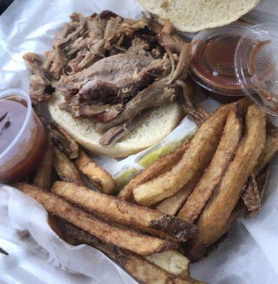 Pulled pork sandwich with fries and a deli pickle.