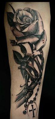 Black and gray realism skeleton hand holding rose with Rosary beads tattoo.