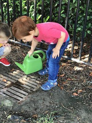 A toddler "play pretend" watering the playground