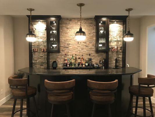 Lighted, open shelf cabinetry and rock wall for back bar in finished basement.