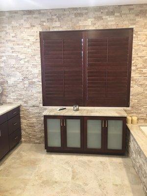 New bathroom with frosted glass towel cabinet, wood plantation shutters, and stone tub and wall surround.