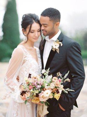 a bride and groom posed in an embrace with a beautiful organic bridal bouquet centered in the frame