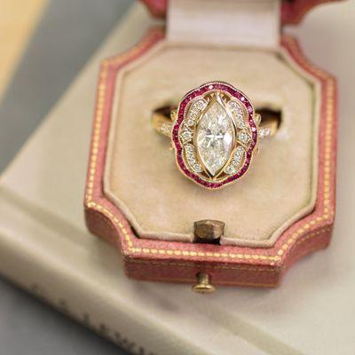 This custom made engagement ring features a marquise cut diamond surrounded by diamond accents and a calibre cut ruby halo.