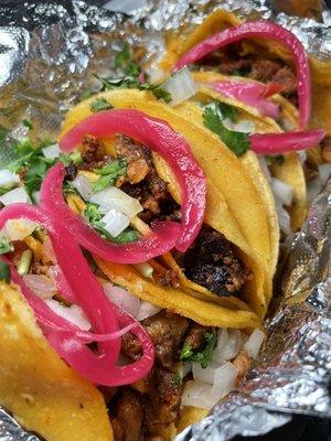 Al pastor tacos topped with pickled onions, white onions, and cilantro