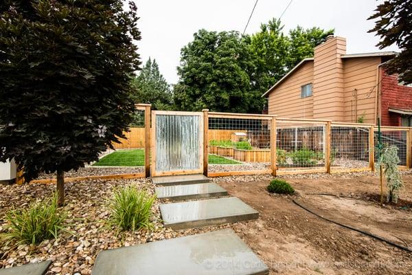 Garden fence with corrugated galvanized metal gate and wire picture-framed panels.