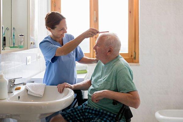 Home Health Aide helping a senior with their personal care by combing his hair