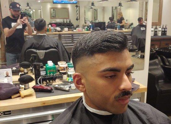 Skin fade with a textured top and mustache trim