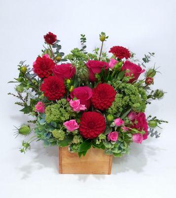 Red dahlias, seedem, green hydrangea, hot pink spray roses, spiral eucalyptus and the different types of greens in a wooden box.