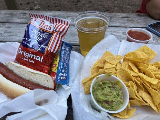 Hot dog, chips, salsa, guacamole, and a Pilsner