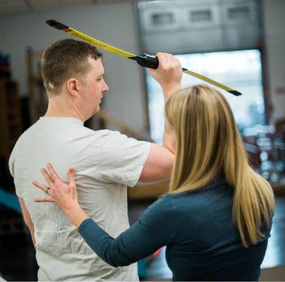 Physical therapist instructing patient in body blade exercise for shoulder stabilization.