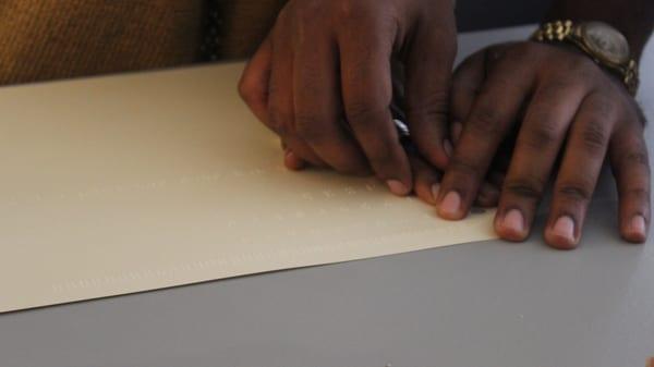 A close up of two hands, one helping the other learn to read Braille.