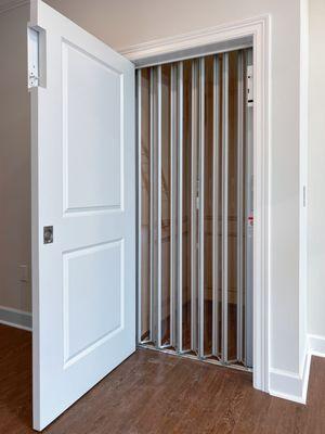 Silver accordion gate with clear accrylic panels for a home elevator.