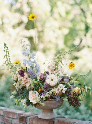 a whimsical flower centerpiece arrangement perched on a brick garden wall with dappled sunlight