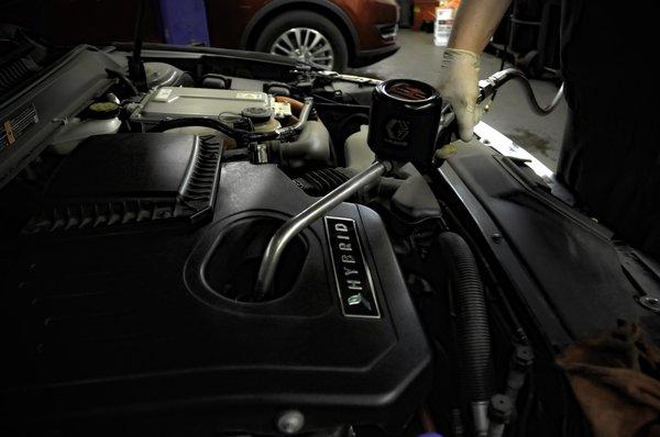 Quicklane Technician filling the engine back up with oil as part of an oil change on this Lincoln Hybrid.