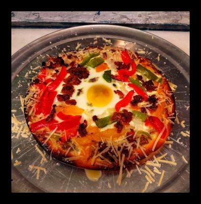 Breakfast pizza with sausage Canadian bacon and regular bacon peppers onions and a fried egg