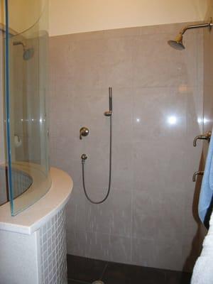 A walk - in shower in a master bathroom features a curved wall with glass. Two shower heads with hand held sprayer included.