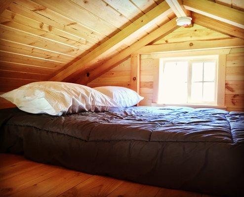 Inside modern cabins. Loft space with fan, outlets, light, and one of two queen beds per cabin that sleeps two.