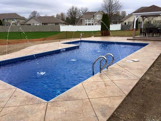 L-shaped inground swimming pool with deck jets and stamped concrete