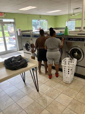 Young, black couple undresses (a bit) and unloads their two-bins full of laundry before leaving it to wash.