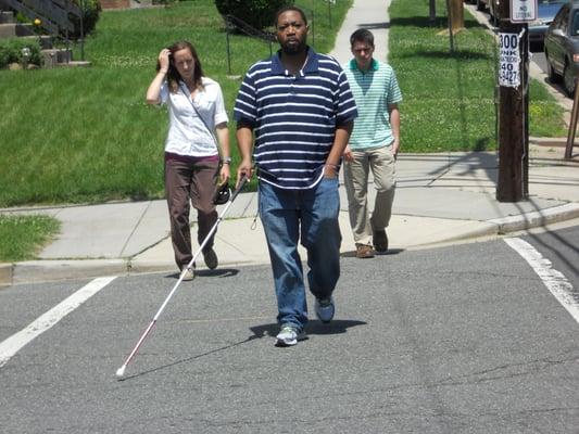 A man using a white cane to navigate a crosswalk.